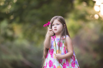 Portrait of a little girl holding hot pink gerbera flower. Outdoor portrait of a toddler girl in bright summer dress, waist up
