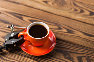 Black metal arm holds orange ceramic mug full of black coffee on old wooden brown table with copy space for your text