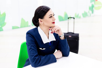 Stewardess with red lips sitting at a table in a cafe in the background travel suitcase