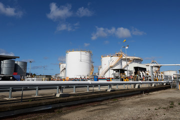 Gas and fuel storage tanks at an oil refinery on a clear day with blue skies and puffy clouds.