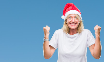 Middle age blonde woman wearing christmas hat over isolated background celebrating surprised and amazed for success with arms raised and open eyes. Winner concept.