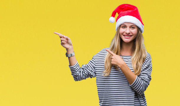 Young beautiful blonde woman wearing christmas hat over isolated background smiling and looking at the camera pointing with two hands and fingers to the side.