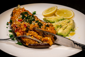 Vegan homemade eggplant, stuffed with quinoa and vegetables, on a white plate with avocado slices and lemon. Aubergine dish ready to be eaten.