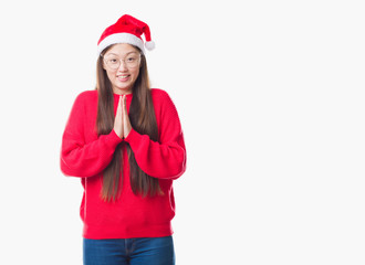 Young Chinese woman over isolated background wearing christmas hat praying with hands together asking for forgiveness smiling confident.