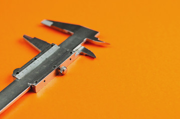 Vernier caliper of gray color on orange table with copy space for your text