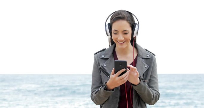 Front view of a happy woman browsing and listening to music on the beach
