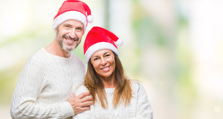 Fototapeta premium Middle age hispanic couple wearing christmas hat over isolated background happy face smiling with crossed arms looking at the camera. Positive person.