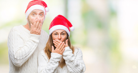 Middle age hispanic couple wearing christmas hat over isolated background shocked covering mouth with hands for mistake. Secret concept.