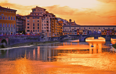 Fototapeta na wymiar colorful buildings, bridge Ponte Vecchio and water reflections in warm sunset on river Arno with small boats in florence, italy