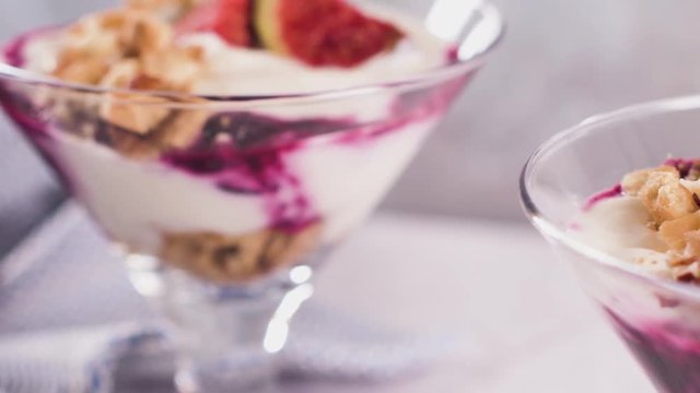Figs pudding parfait with yogurt, blueberry jam, figs, hazelnut, and cookies in glass on white marble background. Flatlay top view.