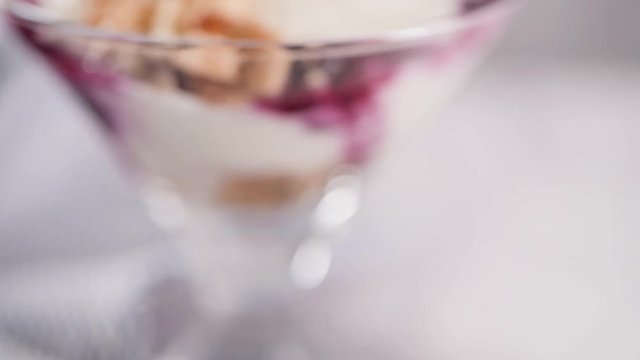 Figs pudding parfait with yogurt, blueberry jam, figs, hazelnut, and cookies in glass on white marble background. Flatlay top view.