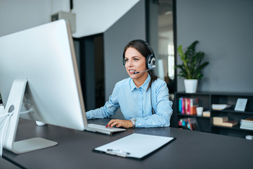 Helpdesk and support concept. Young elegant woman with headset working on computer.