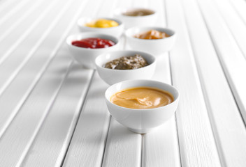 Different tasty sauces in bowls on white wooden table