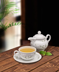 Green tea in porcelain cup and teapot with mint on wooden table 