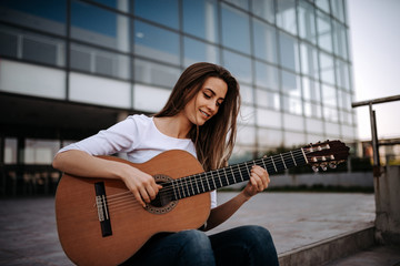 Portrait of gorgeous girl playing acoustic guitar in the city.