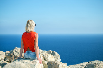  woman sitting on stone on seashore and looking of sea. Vacation and relaxation concept.