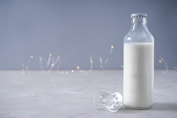 Bottle of milk and pacifier on grey table