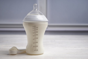 Feeding bottle of milk for baby with powder on white table