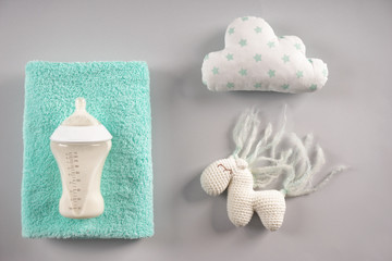 Feeding bottle of milk for baby with towel and toys on grey background