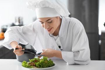 Young female chef dressing tasty salad in kitchen