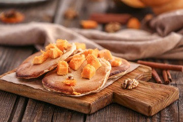Hot tasty pancakes with pumpkin pieces on wooden board