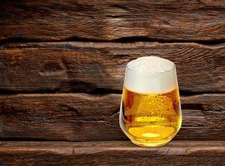 Glass of frothy beer on wooden background