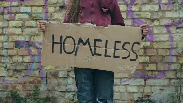 Little Homeless Girl Standing And Holding Cardboard With Sign Homeless On It. Focus On The Cardboard.