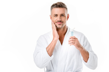portrait of cheerful man in bathrobe using shaving lotion isolated on white
