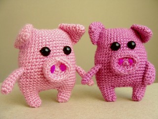 Two pigs crocheted toy with their hands on a light background