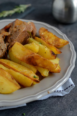 Roast pork with herbs and vegetables on rustic wooden table.