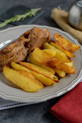 Roast pork with herbs and vegetables on rustic wooden table.