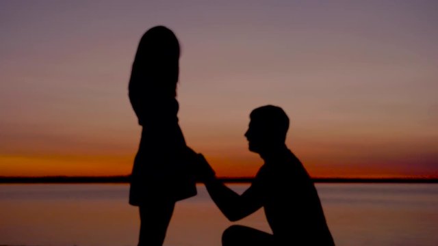 Silhouette Of A Man Sit Down On His Knee And Puts The Ring On The Woman Hand