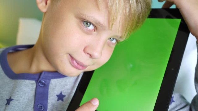 Closeup portrait of cute happy smiling little kid holding black tablet pc in hands close to face. Vertical blank green screen monitor of device can serve as background. REal time 4k video footage.