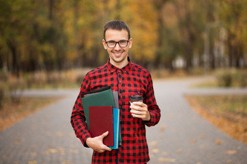 Young student in red checkered shirt with cap of coffee. Portrait of handsome young man holding folders