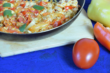 scrambled eggs with vegetables served in a pan for breakfast on dark blue background with tomatoes Bell pepper. copy space top view. omelette