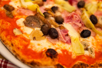 Close up view of a pizza, with olive, ham and artichoke topping