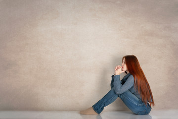 Full length profile portrait of a young woman wearing  blue sweater with long red hair against a beige background in the studio. 