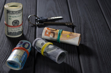 Two rolls of hundred-dollar bills, a fifty-roll roll, a twenty-euro roll tied with rubber bands on a black wooden table