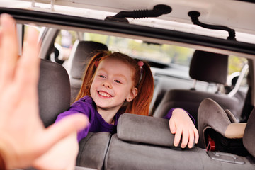 little baby cute cheerful girl with red hair peeking out of the luggage compartment of the car. Family trip