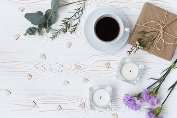 Obraz na płótnie Canvas Top view of coffee, gifts wrapped in kraft paper , hearts, candles, flowers on white wooden table. Background with free space for text. Flat lay