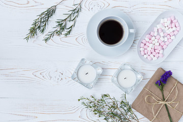 Top view of coffee, gifts, marshmallow, candles, flowers on white wooden table. Background with free space for text. Flat lay