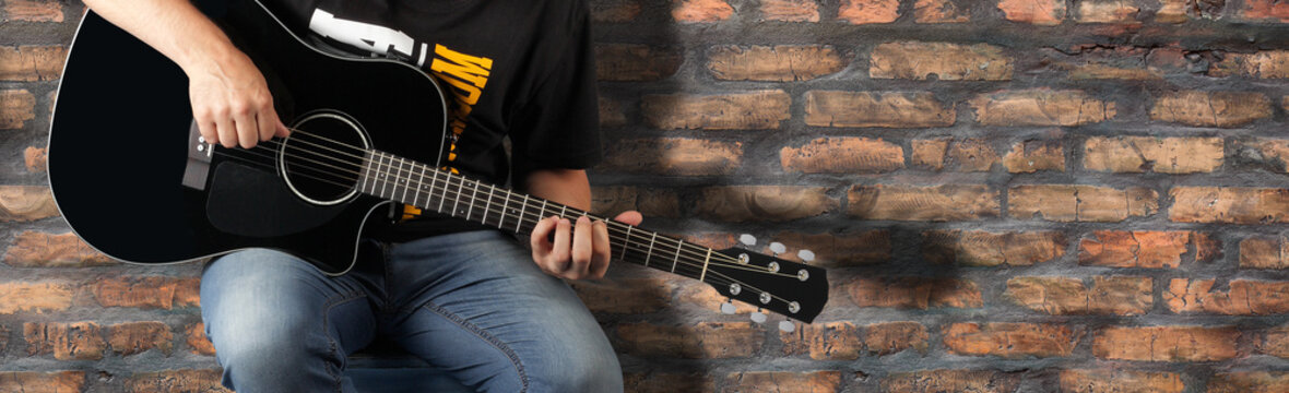 Music - Fragment Man play a black acoustic guitar old brick wall background