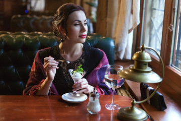 Woman in cafe eating ice cream and looking dreamily out of the window.