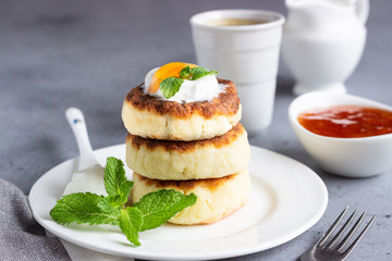 Cottage cheese pancakes or fritters with jam, natural yogurt or sour cream and mint. Traditional Ukrainian and Russian cuisine. Syrniki. Healthy and diet breakfast.