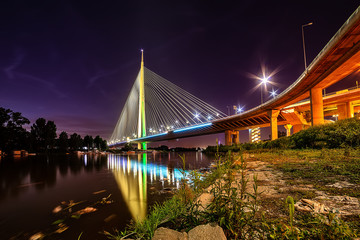 Fototapeta na wymiar Belgrade, Serbia - 20 June, 2018: Side view of Ada bridge at night with reflection over Belgrade marina on Sava river