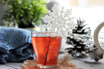 Christmas background - Transparent mug with herbal tea and a beautiful snowflake on the rim, next to a sweater and cones