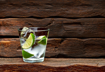 Gin tonic or tequila with lime wedges on wooden table and background