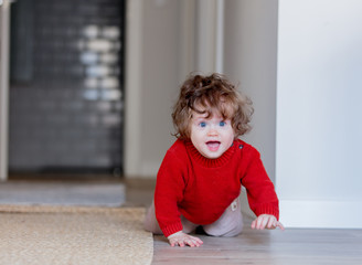 little toddler boy on a floor at home. Wearing in red sweater