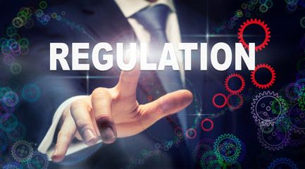 A businessman pressing a Regulation business concept on a graphical display of cogs