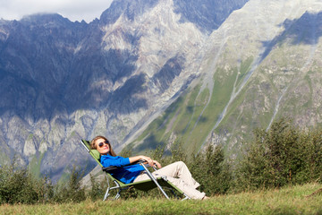 Beautiful blonde sitting on a sun lounger in the mountains. Concept: mountain tourism and mountain travel.